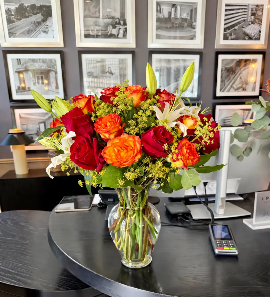 Evening Ember arrangement with red and orange roses, ivory lilies, golden accents, and greenery in a clear glass vase by a Santa Monica florist