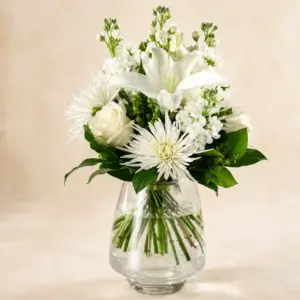 Ivory Bloom white flower arrangement with white lilies, roses, spider mums, seasonal accents, and greenery in a clear glass vase by a Santa Monica flower studio.