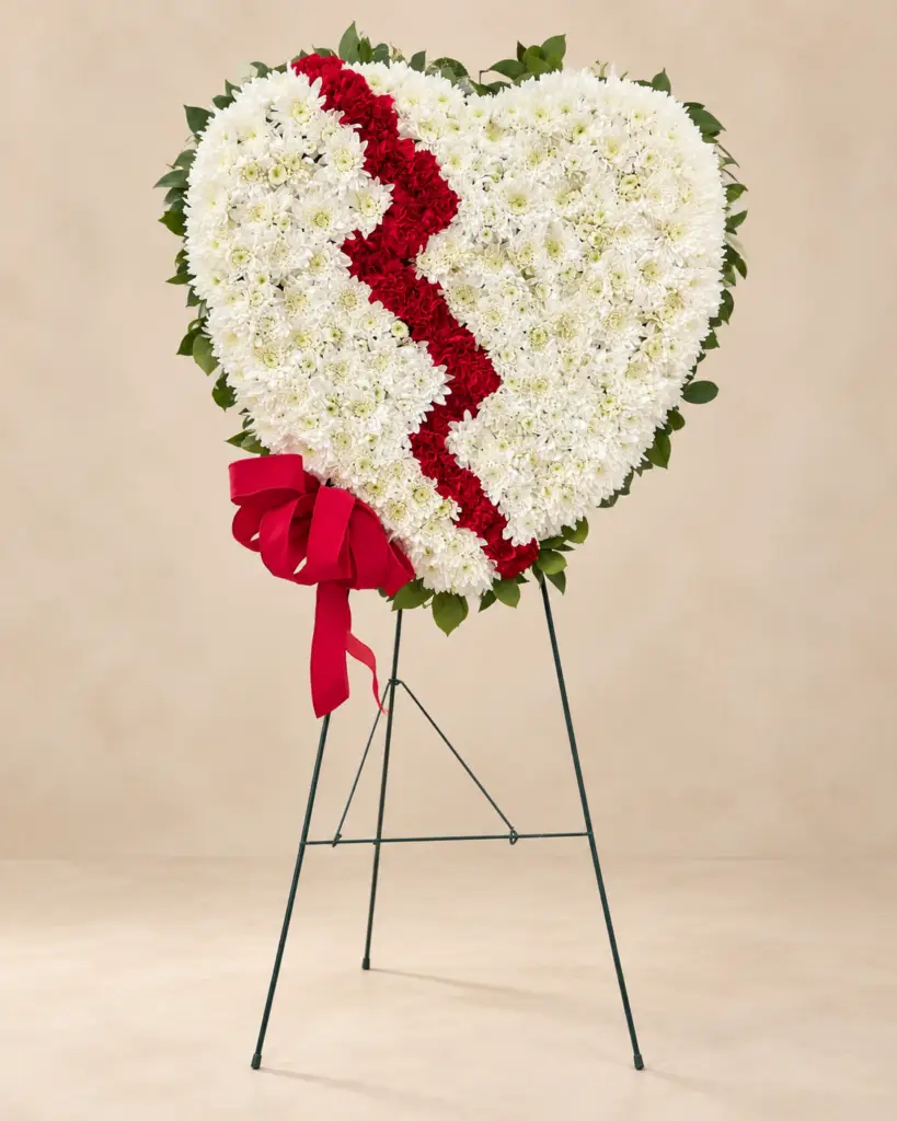 Broken Heart standing funeral tribute with white chrysanthemums, a red floral center, red ribbon bow, and greenery by a Santa Monica florist