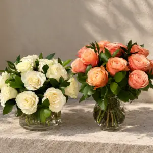 White and peach rose arrangements with fresh greenery in clear glass vases against a neutral editorial background.